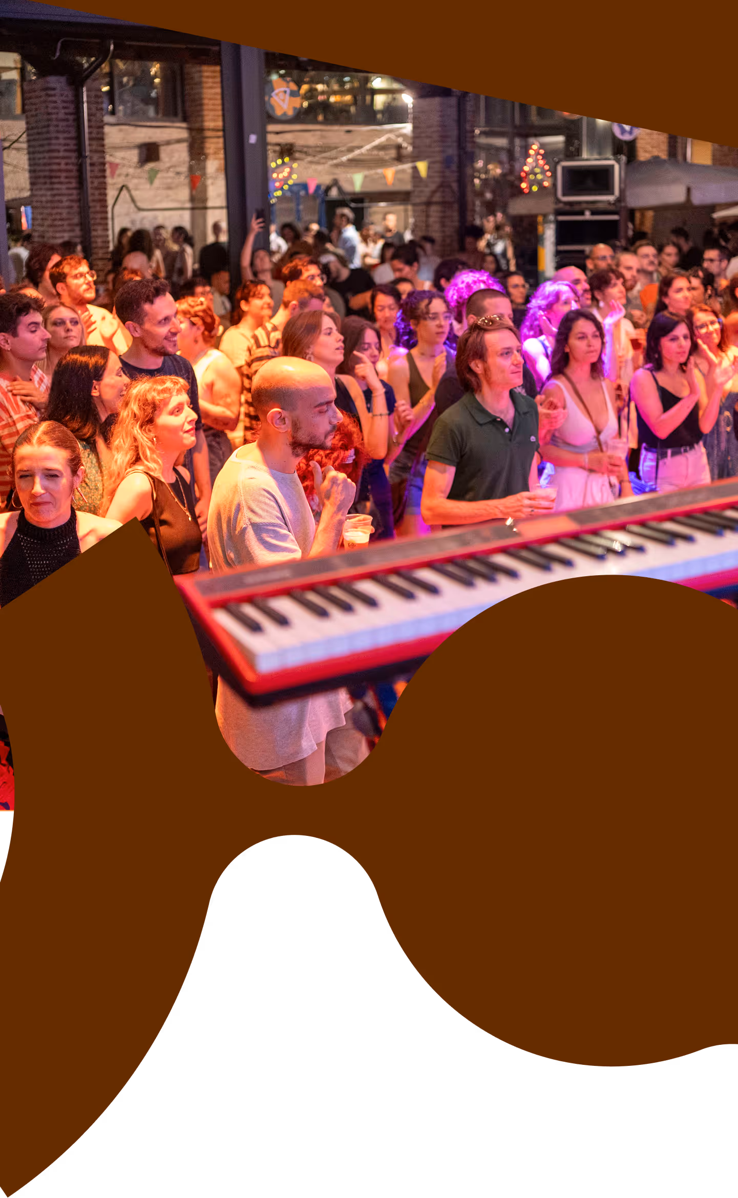 Crowd of people at a lively indoor music event with colorful lighting and a keyboard in the foreground.
