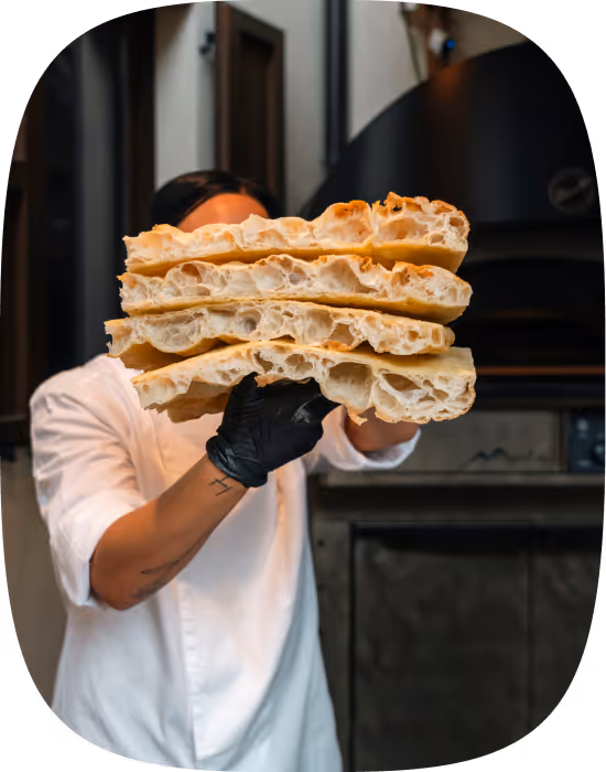 Chef holding up four large slices of bread with airy texture in a kitchen.