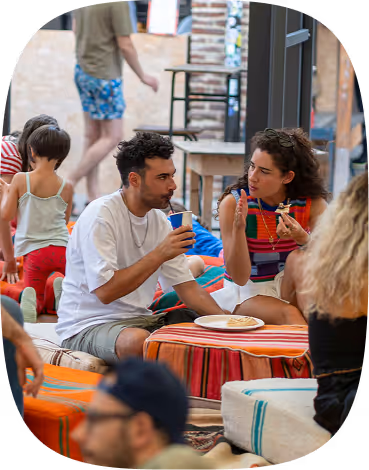 Two people sitting on cushions at a low table, eating and drinking, engaged in conversation.